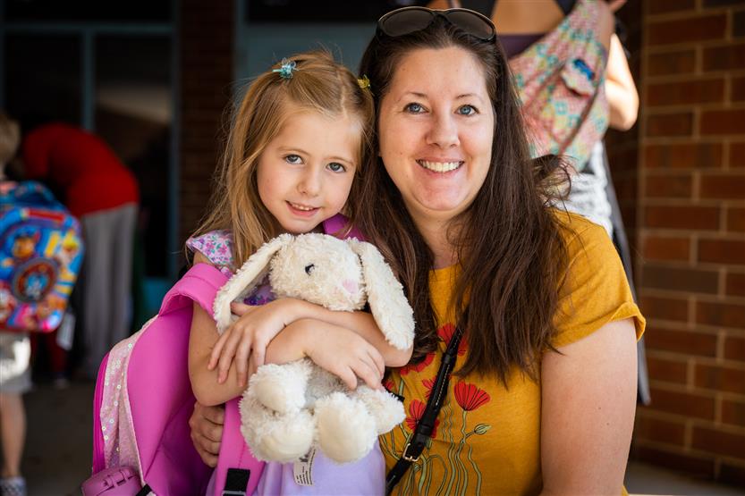A mother hugs her daughter as her daughter hugs a stuffed rabbit
